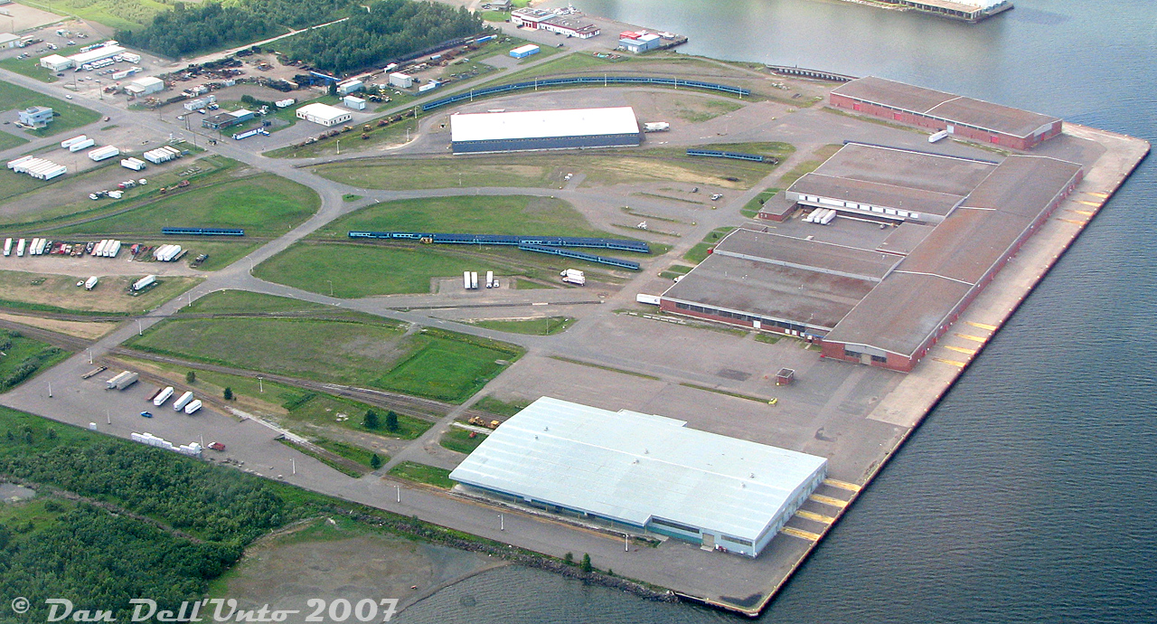 Here's a treat for VIA passenger car fans: all 33 of the unused Nightstar passenger car shells, that never joined VIA's Renaissance fleet, stored in Thunder Bay on various tracks around Keefer Terminal. Most are visible in small groups stored on the various tracks (I count 29), but 4 are hiding behind one of the warehouses on the upper right. Some maintenance of way equipment is also visible scattered here and there.

A total of 139 cars built for the proposed-but-not-realized UK "Nightstar" overnight service through the Channel Tunnel were acquired by VIA Rail in 2000, after being built and stored for a number of years. As I understand it, there was some political pressure to purchase these cars for a song, but there were a number of compatibility issues between them and North American rail standards. They were sent to Thunder Bay where 106 were modified by Bombardier into various types of cars to operate in VIA service as their "Renaissance" fleet. The 33 remaining shells were stored here at Keefer Terminal near the Bombardier plant for possible future conversion, but no further cars were ever needed or rebuilt. 

The stored cars languished here until they were removed from Keefer terminal a year later in August 2008, lifted from their trucks, and then stored in a field nearby. All were then cut up for scrap.