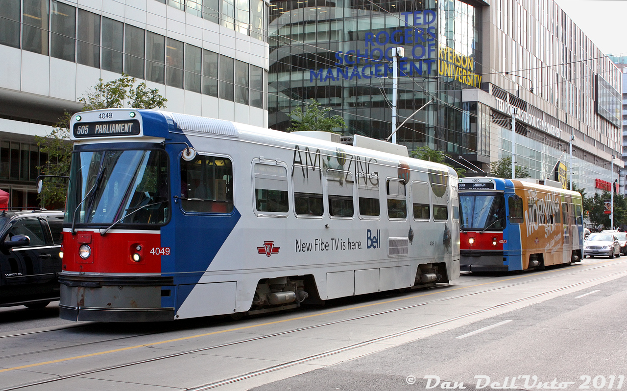 TTC CLRV's 4049 and 4070 bunch together like only Toronto streetcars can on two 505 Dundas runs, heading eastbound on Dundas Street approaching Yonge Street in the busy and bustling Yonge-Dundas Square area. The first car appears to be short-turning at Parliament Street (named after the original location of Parliament in the olde Upper Canada daze), while the unfortunate souls riding behind will be short-turned at Church to redeem themselves. The two streetcars are excellent specimens of the many wraps featured on the CLRV fleet over the years: 4049 wrapped for Bell Fibe TV, and 4070 wrapped for Global Toronto's The Morning Show with Liza Fromer (tune in Weekdays 6-9!).They're passing Ryerson University's (they hate it when you call it that) Ted Rogers School of Management, the crown jewel of Rye's High's Faculty of Business built in 2005-06 on the site of a former Eaton Centre parking garage at Bay and Dundas, and replacing the old and mediocre Victoria building that was previously used by the business school (I've heard the stories from classmates...just a generally outdated building equivalent to attending a high school, nothing like poaching rats in the basement for extra credit or anything).Open for business* in the fall of 2006, bragging rights at the time were that Ryerson finally had a proper "Business School on Bay Street" to compete with the likes of UofT's Rotman School of Management and York U's Schulich (I did attend there once - to use the washrooms, it was nice). For the first two years or so the new facility operated as the Ryerson Business Building (RBB), until a wheelbarrel full of cash rolling down Bay Street tipped over in front of it, and then it became the Ted Rogers School of Management (TRSM) in 2008 or so. It shared the building with commercial retail on the ground level including Canadian Tire, Best Buy, and Mark's Work Warehouse, and has since remained the TRSM after the TEMU U rebrand. most of the reviews are positive, so they must be doing something right.*Pun intended.
