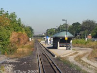 A nice view of the old Weston GO Station, very quiet and very quaint surrounded by lush greenery, until it was replaced by a brand new station to the south a few years later and subsequently obliterated by a giant grade-separation trench. The view today is from the <a href=https://www.railpictures.ca/?attachment_id=59189><b>rear of GO Transit cab car 237</b></a>, departing on morning train #252 enroute to Union Station downtown. In the distance are the grade crossings for <a href=http://www.railpictures.ca/?attachment_id=59215><b>John</b></a>, King, and <a href=http://www.railpictures.ca/?attachment_id=8995><b>Church Streets</b></a> before the Weston Sub curved to the west and crossed the Humber River bridge at <a href=https://www.railpictures.ca/?attachment_id=59244><b>CN McGill</b></a>. <br><br> This station was the original built by GO Transit for the launch of their <a href=http://www.railpictures.ca/?attachment_id=30566><b>new Georgetown line</b></a> in April 1974, and replaced an <a href=http://www.railpictures.ca/?attachment_id=51315><b>old CN station</b></a> that was previously here (demolished 1966). It did incorporate the old CN waiting room building that managed to survive. Like <a href=https://www.railpictures.ca/?attachment_id=59667><b>Bloor GO Station</b></a>, the amenities here were also sparse, with some shelters, a small rectangular insta-station building, its own payphone (thanks Ma Bell) and an underground tunnel at this (south) end of the platform going under the tracks and coming out along the Lawrence Avenue underpass below (note bridge railings). The <a href=http://www.railpictures.ca/?attachment_id=11144><b>north end of the platform</b></a> fronted onto John Street, where a very small GO parking lot was shoehorned in nearby almost as an after though. The odd platform shape at this end was for a CN service track that had previously run along the back of the station and connected to interchange tracks along CP's MacTier Sub on the right (incidentally, there was a CN-CP connecting track still present just to the south of here). <br><br> The demise of this incarnation of Weston Station came about with the idea for a new "Blue 22" Pearson airport express train (initially planned to use rebuilt RDC cars from IRSI) and expanded all-day two-way Georgetown corridor GO service with the West Toronto grade separation happening. Both would have required an updated, modernized station on site, although the UPX wasn't originally supposed to stop at Weston. The residents of Weston weren't happy about all of this, and launched a grassroots campaign targeting "Dalton's Dirty Diesels" (after then-Ontario premier Dalton McGuinty, more on him in a future post) due to all the extra diesel trains that would be running through the corridor on the expanded GO and new UPX lines. Among other things they wanted electric trains, a stop at Weston, and a grade separation for the about-to-be-busier rail corridor (that already intersected their neighbourhood for decades dating back to the steam era). <br><br> Only two of those three demands were met: they got their trench from Metrolinx, and their UPX stop in the form of a new Weston station that opened in stages between 2013-2015. There was lots of talk about electrification and pushing for studies, including planning to do the section of the corridor for the UPX line and a stretch from Union to Mimico so the UPX trains could be serviced, and possible servicing facilities at <a href=https://www.flickr.com/photos/51593483@N06/49577632097><b>Humberview</b></a>. The RDC idea was replaced with new <a href=http://www.railpictures.ca/?attachment_id=45648><b>Nippon Sharyo DMU trainsets</b></a> with Tier 4 emissions diesel engines. This was also part of why GO sent an MP40 down to MPI for <a href=http://www.railpictures.ca/?attachment_id=21611><b>Tier 4 conversion</b></a> into an MP54, as "Tier 4" and "clean diesel" were some of the PR-friendly terms thrown about to appease the residents (since all the studies and implementation of electrification wasn't practical or possible in the given timeline for many reasons). Ultimately nothing really became of it, as after the trench went in and the new efficient UPX service started up, the residents soon forgot about electrification and everything quieted down. <br><br> Someone else had the last laugh though: after all that work, CP's MacTier Sub was left fully at-grade next to the trench, forcing residents to keep waiting for long CP diesel freight trains to pass through.