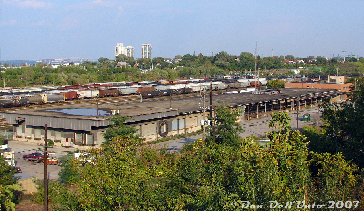 An overhead overview of CN's old Hamilton freight sheds, out of use for a number of at the time of this photo, located adjacent to the CN/Southern Ontario Railway's Stuart Street Yard. The main offices were in the brick portion on the right, while the bulk of the building was warehouse space with truck loading docks. Four rail sidings (two on each side, some still visible) ran along both sides of this end of the building for spotting boxcars for loading/unloading.According to the informative "Building GO Transit" article by Wilfred Sergeant, as part of the relocation of much of CN's freight yard operations in downtown Toronto, Mimico and Danforth to Vaughan in the 1960's (the new Toronto/MacMillan Yard), their downtown express and LCL operations were to be consolidated from their old Simcoe Street LCL freight sheds (along Front Street, near CP's own sheds) and the express building adjacent to Union Station into a new, modern, larger express-freight facility located within the new yard up in Vaughan (known as Maple). This was due to a study at the time that found many shippers were moving their operations out of the downtown area to new industrial areas and business parks being developed in the suburbs along Highway 7.The new Maple express/freight shed was also to feature new modern automated sorting processes and equipment. In order to test and refine this, a smaller test shed was built here in Hamilton and outfitted to test and refine the new technology and processes that were to be implemented in Maple. It replaced some of the older local freight/express facilitiesAs per other notes and photos by Doug Page, the Hamilton shed was built in 1964 (on the site of the old CN Hamilton roundhouse), and closed in 1997. By the time of this photo in 2007 it was vacant, and two years later in 2009 it would succumb to the wrecking ball.