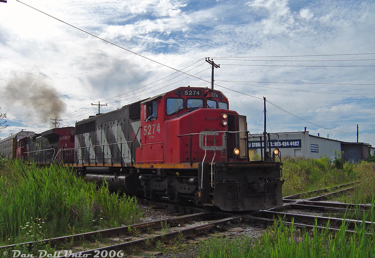 After waiting at the signals to the west for GEXR #431 to clear the single track section of the Halton Sub between Brampton East and Peel, CN SD40-2W 5274 and C44-9W 2587 throttle up and proceed through downtown Brampton, thumping the diamond with the ex-CP OBRY Owen Sound Spur just west of Brampton Station and "Beating the GO Rush" before the first Georgetown-line GO train shows up around 5pm.

At the time the downtown Brampton area of the Halton Sub had a bit of a vegetation overgrowth problem (much to the detriment of photographers), that would later be fixed when CN dug up the area to upgrade the signals around the diamond, and began clearing land to double- and triple-track parts of the Halton Sub through Brampton during the next year. The building in the background used to be an old Pease Swift foundry many years ago (with a siding off CP), before its current use as a self-storage facility. The OBRY would discontinue all operations in December 2021, and the end finally came for the old Brampton diamond when it was ripped out in July 2024. Hard to believe there was once even an interlocking tower here controlling traffic until 1958!