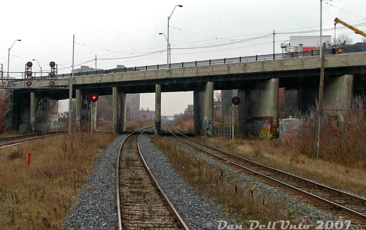 After departing our final station stop before downtown Toronto, we're picking up speed on the jointed rail stretch of the Weston Sub between Bloor GO (in the distance) and CN Parkdale on the home stretch to Union Station, zipping under the Dundas Street West overpass on the way out of West Toronto. The northbound advance signals to the diamond at West Toronto are visible on this side of the bridge, that was undergoing some rehabilitation work at the time (including a new handrail recently installed).

The track on the left is the double track CP Galt Sub running parallel down the rail corridor, this location being known as CP Dundas in employee timetables. On the right, CP's old TG&B "Bruce Service Track" (now removed) once used to duck under the bridge and go to the Compressed Metals scrapyard just south of Dundas. The track continued out the other side as a CN siding (see middle of 1971 aerial here). On the north side of the bridge to the right is the Nestle chocolate factory, once home to Cowan's Chocolates, off Sterling Road (apparently sugar from Redpath downtown was shipped here via hoppers). Just a stone's throw away, the Newmarket Sub ducked under Dundas below its own bridge.

To the left in the distance are the two towers of The Crossways Mall at Bloor and Dundas.
