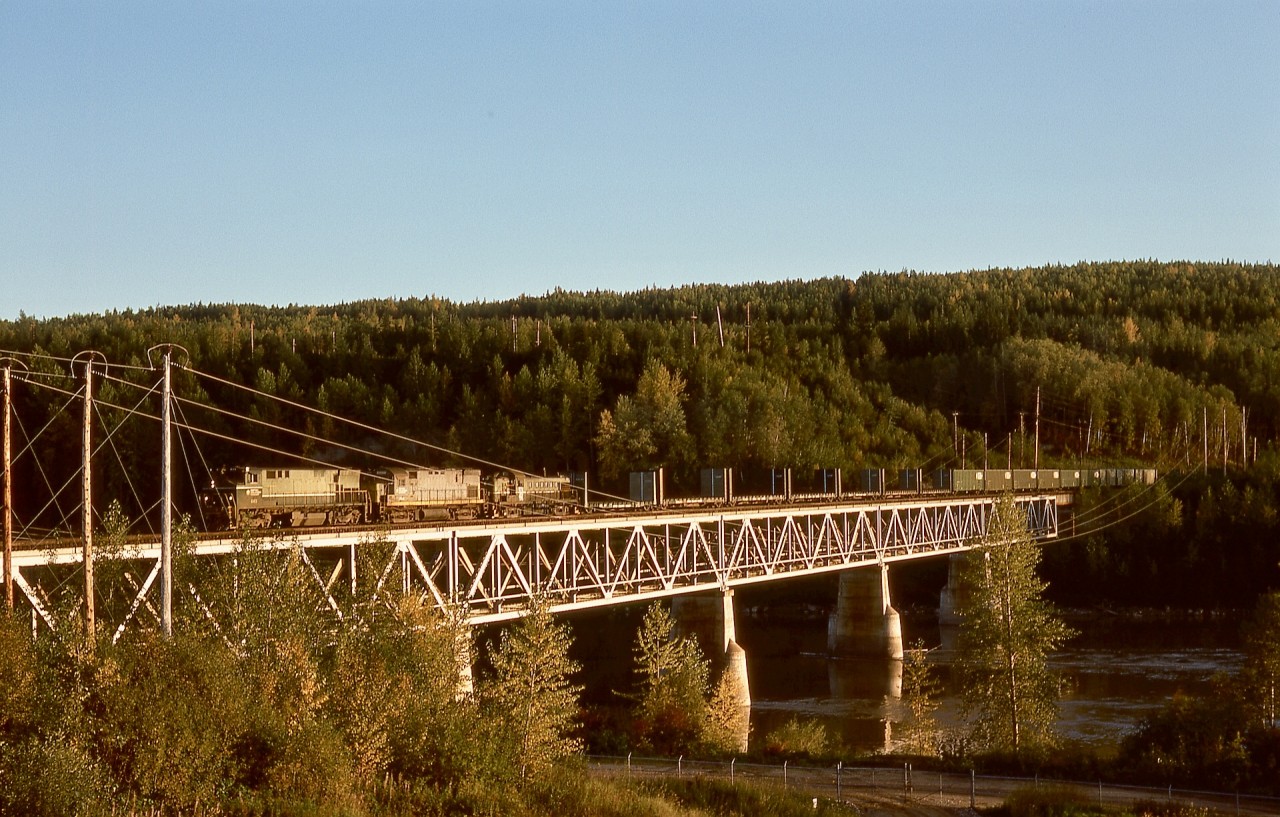 Northward from Prince George, the British Columbia Railway crossed the Fraser River one last time to reach Bridge yard serving pulp mills and onwards to Peace River country.  On Friday 1976-09-17 at1825 PDT, that bridge was utilized by a northward train of empties, powered by BCOL 643 + 806 (ex Erie Lackawanna 2456) and PGE 576 not yet repainted.