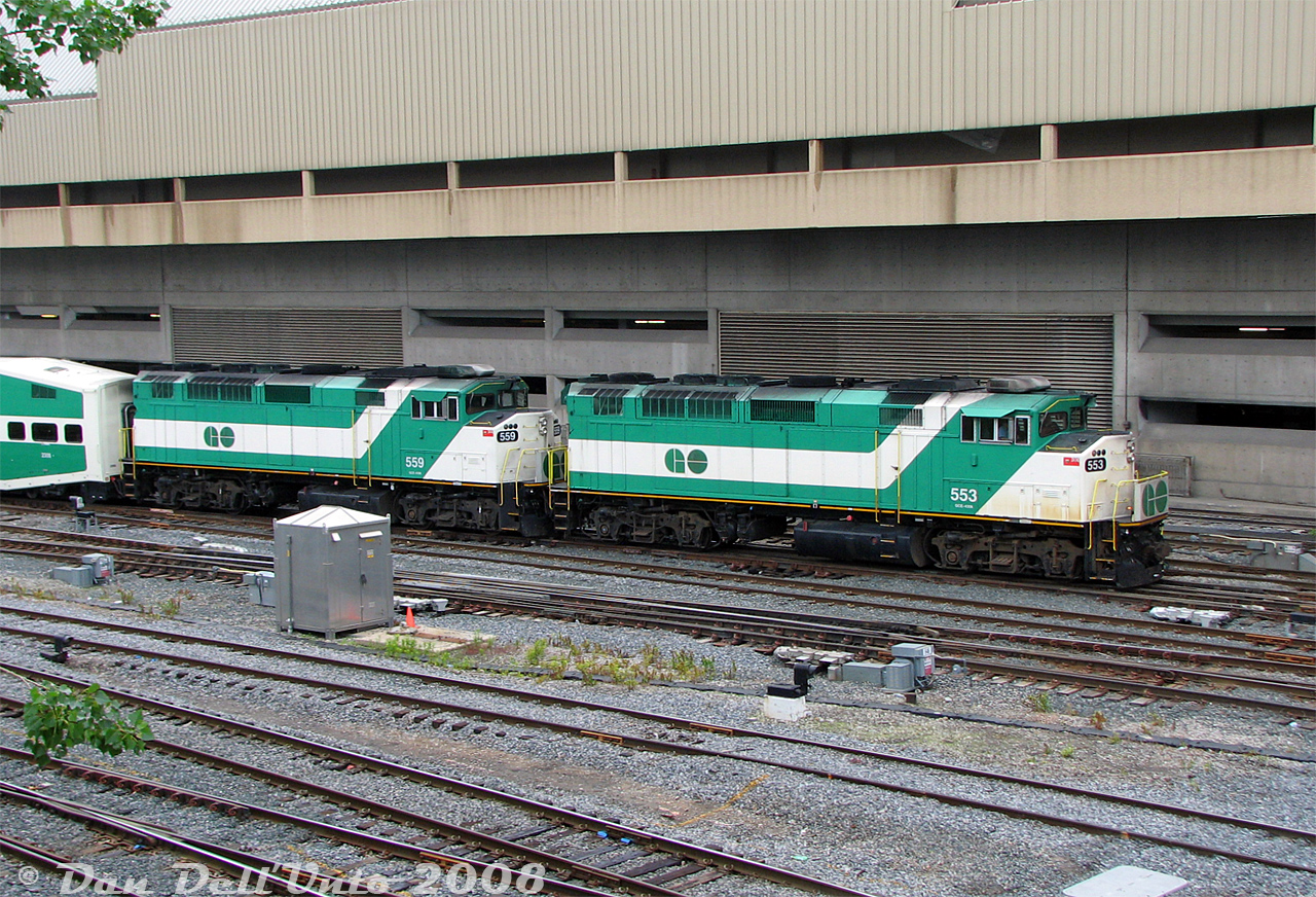What's better than one GO Transit F59PH? Twins! GO 553 and 559, part of the same 1990 order from GMD (548-561), arrive inbound at Toronto Union Station with afternoon Lakeshore line train #912. The double F59's were mostly used for weekend Lakeshore runs, but a consist or two would often make it onto the weekday equipment cycle.Becoming familiar with GO's equipment cycling made it easy to catch triple the afternoon trains in one visit: at the time there was an afternoon equipment change-off for two of the all-day Lakeshore line runs. This consist as #912 would arrive then depart Toronto to eastbound to Oshawa as usual, and come back as #917 only as far as Union Station. Another new consist would be waiting at Union, deadheaded from Willowbrook, to take over from #917 on the adjacent platform. Once the passengers had transferred trains, the new consist as #917 (today with F59PH 560) would depart in service, and the previous #917's consist would deadhead to Willowbrook as an equipment move. The same thing happened with another new consist taking over for train #919 an hour later.Knowing all this, it was easy pickings shooting the new equipment move inbound from Willowbrook, it departing westbound as the new in-service train, and the old consist departing out-of-service for Willowbrook. Twice, if you wanted to wait the extra hour out.