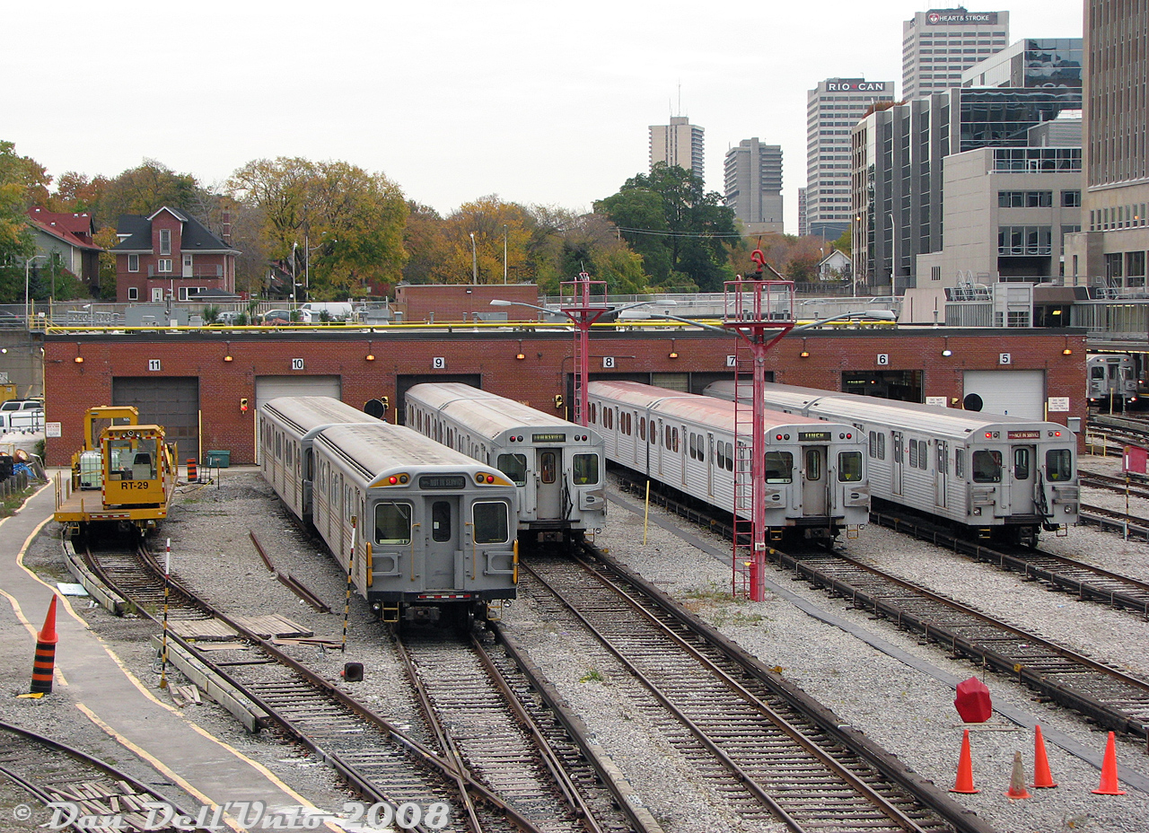 A nice selection of TTC subway equipment is pictured lined up outside the shops building at Davisville Yard, all typical cars serviced at Davisville at the time. From left to right are TTC flatcar (work car) RT-29, TTC H4 work cars RT-65 and RT-64, two sets of H5 subway cars, and a set of T1's. On the far right, the front car of a train of yet H5 cars sits on the third platform at Davisville Subway Station at Yonge and Davisville (with the midtown Toronto skyline along Yonge near Davisville-Eglinton visible in the distance).Davisville Yard was the TTC's original 1950's maintenance base for the newly opened Yonge Subway line, but by this point in time shared Yonge-University-Spadina line equipment with the larger and more modern Wilson Yard. The H5 cars were strictly operated on the YUS, while the T1's handled the YUS and Sheppard Subway duties. The other two remaining revenue classes (H4 and H6) were assigned to Greenwood Yard for Bloor-Danforth line service with the older T1's.There were two rail attractions to visit in this area of Toronto: the TTC Davisville Yards from this vantage point off the Kay Gardner Beltline Trail (the old CN Belt Line Branch off the Newmarket Sub, that the city purchased in the early 1970's and turned into a popular walking trail) and the original George's Trains nearby, along Mount Pleasant near Davisville.