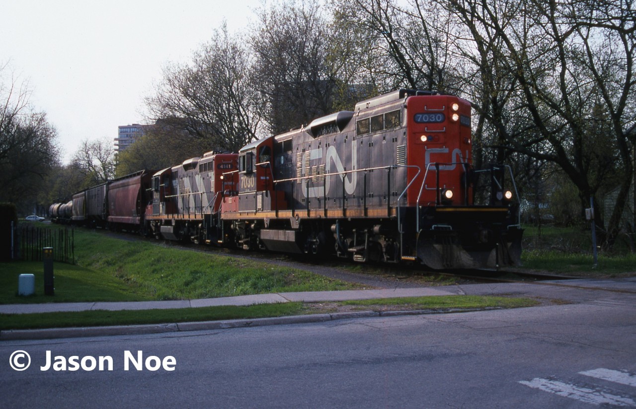 The CN 15:30 Kitchener Job is pictured approaching John Street in Waterloo, Ontario as they return from Elmira with seven cars on the Waterloo Spur with 7030 and 4141. At the time, the job only operated with two units when it was necessary and on this day, both Nutrite and Sulco Chemicals in Elmira had received several cars. The springtime was always a busy period for Nutrite receiving hoppers.