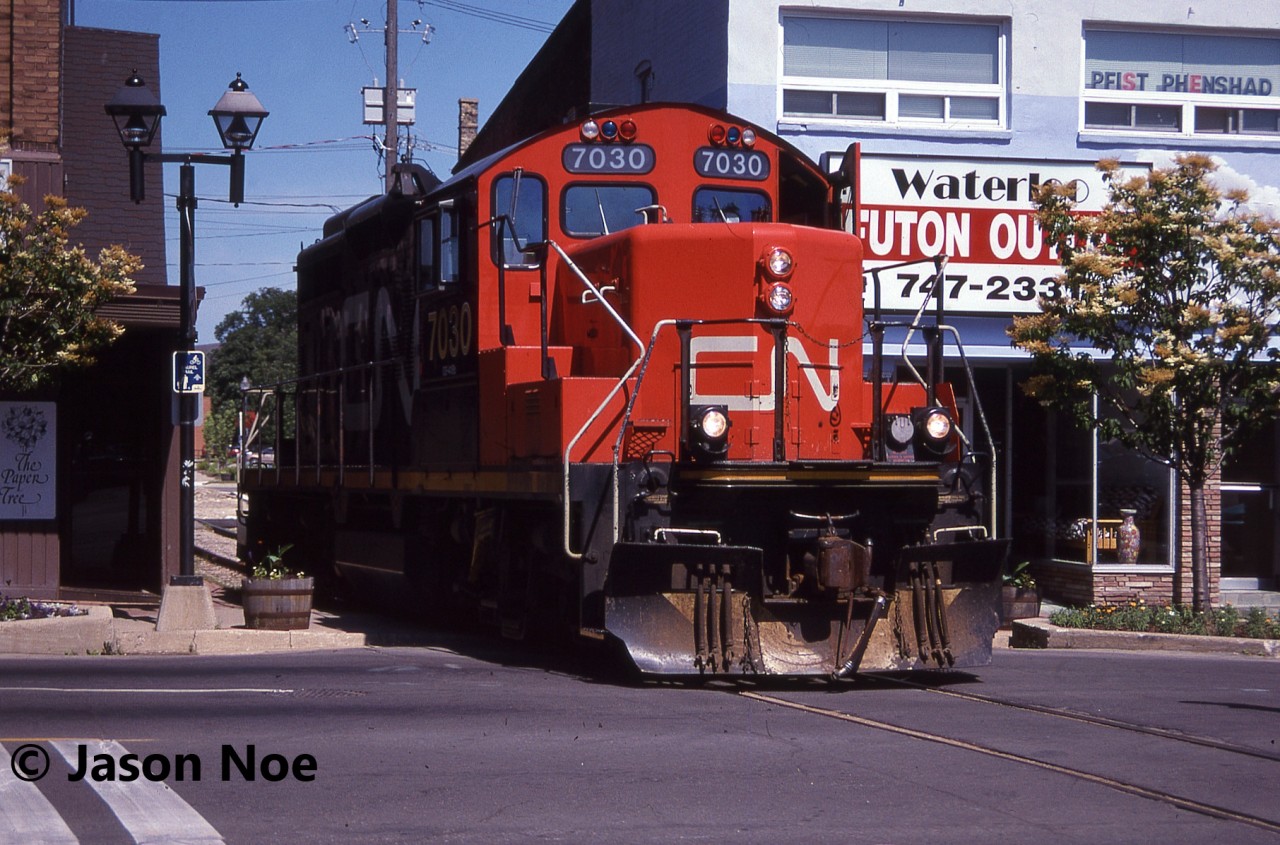 The CN 15:30 Kitchener Job with GP9RM 7030 makes a mid-afternoon appearance in downtown Waterloo, as the crews heads to the town of Elmira, Ontario on the Waterloo Spur light power. Often during the month of July in the 90’s, with the Budd Plant in Kitchener slowing production for summer shut down, they didn’t require CN service daily, so the 15:30 Job would head to Elmira earlier in the afternoon rather than later in the evening.