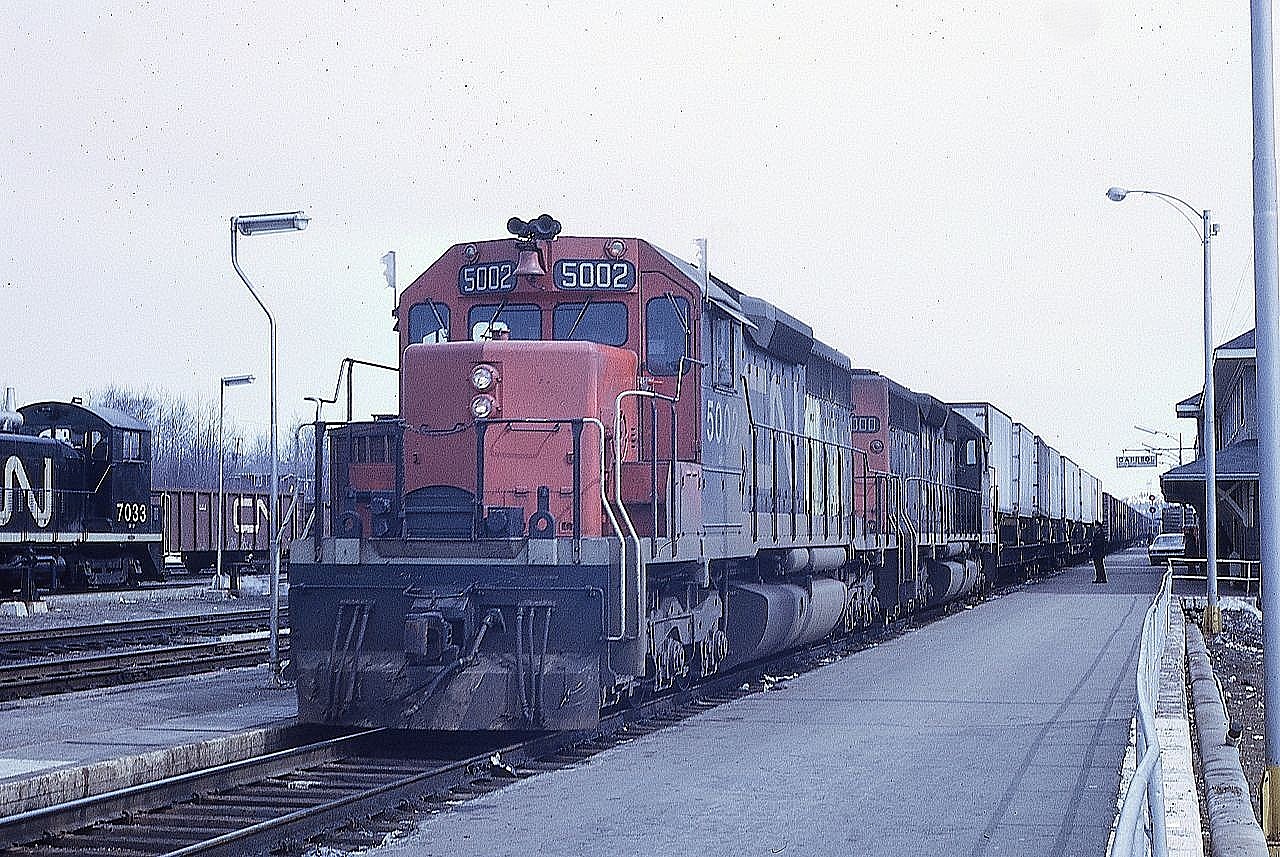 Two of CN's first three SD40s, 5002 and 5000, lead train 301 down the main line at Capreol, Ontario under the watchful eyes of a CN Police officer.  SW1200 7033 sits on spot on track 2R.