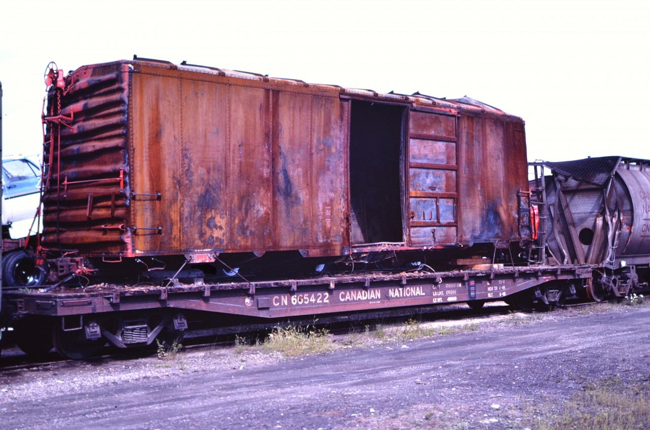 Hot box!  
An unknown road's box car is secured to the deck of CN 665422 and sits in CN's Hornepayne, ON yard after being moved from Cree Pit just south of town with a string of other wreck damaged equipment.