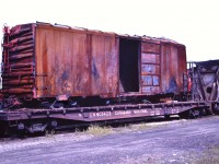 <b> Hot box! </b> <br>
An unknown road's box car is secured to the deck of CN 665422 and sits in CN's Hornepayne, ON yard after being moved from Cree Pit just south of town with a string of other wreck damaged equipment. 
