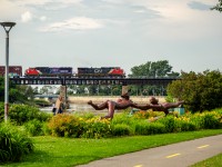 CN 402 crosses the bridge over the Rimouski river with SD75IACC #8357 in trail, a locomotive specially painted for suicide prevention. In the foreground is the sculpture titled La Rencontre Sous-marine, by local artist Roger Langevin. The bridge over the river was first built by the Intercolonial railway in the early 1870s, the girders were later replaced in the early 20th century.