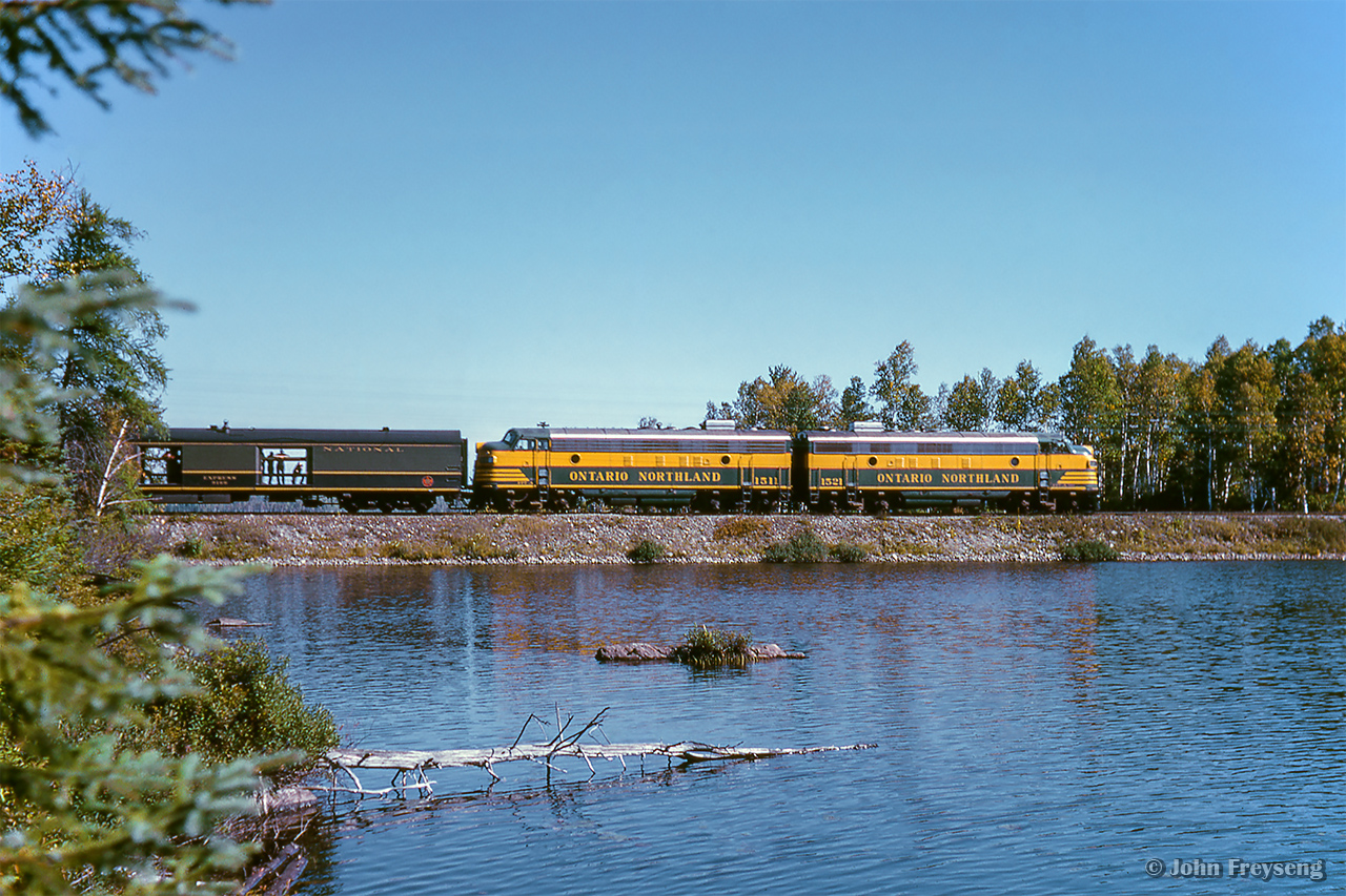 The weekend of September 13 - 15, 1963 marked a massive undertaking by the Upper Canada Railway Society, a 692.2 mile excursion from Toronto - Ottawa - North Bay - Temagami - Toronto, with seventeen coaches behind CNR 6167. With the train having run overnight from Toronto - Ottawa on the 13th, the train turned west and departed the nation's capital early on the 14th, running across northern Ontario to North Bay. 6167 would be removed at North Bay, with ONR FP7s handling the train to Temagami overnight. The consist returned to North Bay on the morning of the 15th, with 6167 taking over once again for the return to Toronto.

About halfway back to North Bay from Temagami, passengers have detrained for a runpast, as the pair of green and yellow FP7s rumble past Moose Lake at approximately mile 28, just north of the community of Tomiko.

Further information can also be found in the December 1963 UCRS news letter.

The saga:
Ottawa Arrival
Ottawa Dominion
CNR 6167 in the capital
Running across the north
Sleek steam
Morning at Temagami
Jocko runpast
North Bay arrival

Scan and editing by Jacob Patterson.