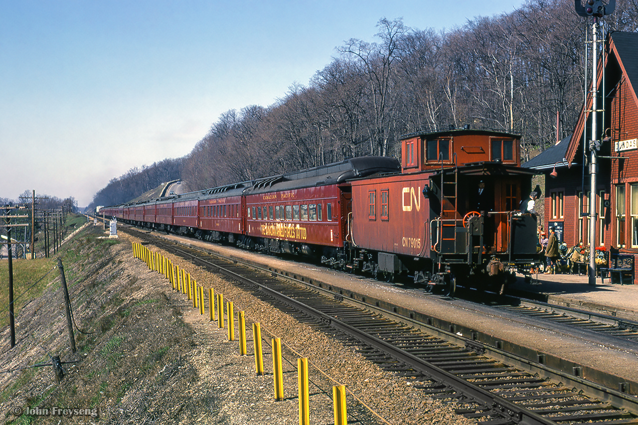 Touring the nation as part of the 1967 centennial celebrations, one of the two trains carrying the Canadian Armed Forces Military Tattoo climbs the grade at Dundas, bound for an evening performance in Sarnia. The tattoo was designed to operate as three parts, with part 1 being the initial tours of the two trains from late March through mid May, performing arena shows with 450 performers. One consist was made up of CN equipment, known as 'train A,' and carried the 'blue' group of performers, while the other was made up of CP equipment, aka 'train B,' carrying the 'red' group of performers. In late May, both groups combined, and additional performers added, bringing the total to about 1700 for the next stage of shows; stadium performances from late May through August. The final part of the tattoo would be smaller shows beginning in late summer, and wrapping up in mid October. Further reading can be found on Keith Allan Wilson's Tattoo 1967 website, as well as the itinerary of events for the year. More photos to come, and more details on this can be found in Tom Henry's article in the April 1967 UCRS newsletter.

Approaching the scene
Mid train

Scan and editing by Jacob Patterson.