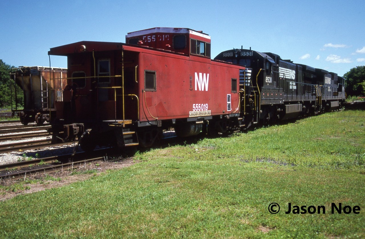 During a hot summer afternoon, Norfolk & Western caboose 555019 along with Norfolk Southern C39-8 8617 and C36-7 8531 await their next call to duty at the CN yard in St. Thomas, Ontario. Van 555019 was one of several NW cabooses assigned to Canada.