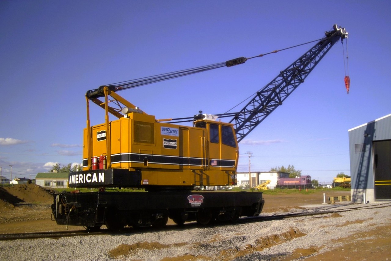 An American arrives in town  
In 2003, QIT (Riviere Romaine Railway) replaced their aging Ohio locomotive crane with a remanufactured American model 855 DEH (Diesel Electric traction, Hydraulic swing) crane. 
It is seen here on July 2, 2003 outside their equipment shop during in-service commissioning. 
In the background you can see locomotive QIT 1 (ex-QIT 4) on static display at the roadside leading into town. Directly across the street from the Hotel Du Havre which was my home for the week.