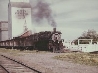 This is a very impressive colored photograph, likely from the 1950s period. CPR 2572 leads a grain train out of Coaldale AB. 