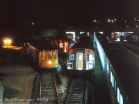 An assortment of TTC subway equipment gathers by the shops at Davisville Yard at night in the Summer of 1963, as seen from the still-active <a href=http://www.railpictures.ca/?attachment_id=45684><b>CN Belt Line Branch</b></a> bridge spanning the yard. The brand new 5300-series MLW M1's were the only aluminum subway cars on the property at the time (the first H1's wouldn't arrive <a href=http://www.railpictures.ca/?attachment_id=32616><b>until 1965</b></a>), and they're mingling with the original "Red Rocket" steel <a href=http://www.railpictures.ca/?attachment_id=43138><b>Gloucester "G" cars</b></a> built in the 1950's, dating back to the 1954 opening of the Yonge line. The University subway line had opened earlier in the year, and "St. George" on the M1's rollsign reflects the new western end terminus of the combined Yonge-University line (no Spadina extension <a href=http://www.railpictures.ca/?attachment_id=36309><b>until 1978</b></a>). Yellow-painted work equipment lingering around includes RT-4, former Peter Witt streetcar 2528 converted for garbage collection on the subway, and an unknown dump car behind (possibly RT-3).<br><br>For a more modern 2008 view of this area of Davisville Yard: <a href=https://www.railpictures.ca/?attachment_id=59740><b>https://www.railpictures.ca/?attachment_id=59740</b></a><br><br><i>Original photographer unknown, Dan Dell'Unto collection slide.</i><br><br>Note: the photographer of this image is unknown, but judging from the labeling and date stamp, they also took photos of <a href=https://www.railpictures.ca/?attachment_id=46591><b>streetcars at Bloor</b></a> and <a href=http://www.railpictures.ca/?attachment_id=38483><b>CP near at West Toronto</b></a> on their 1963 visit to Toronto.