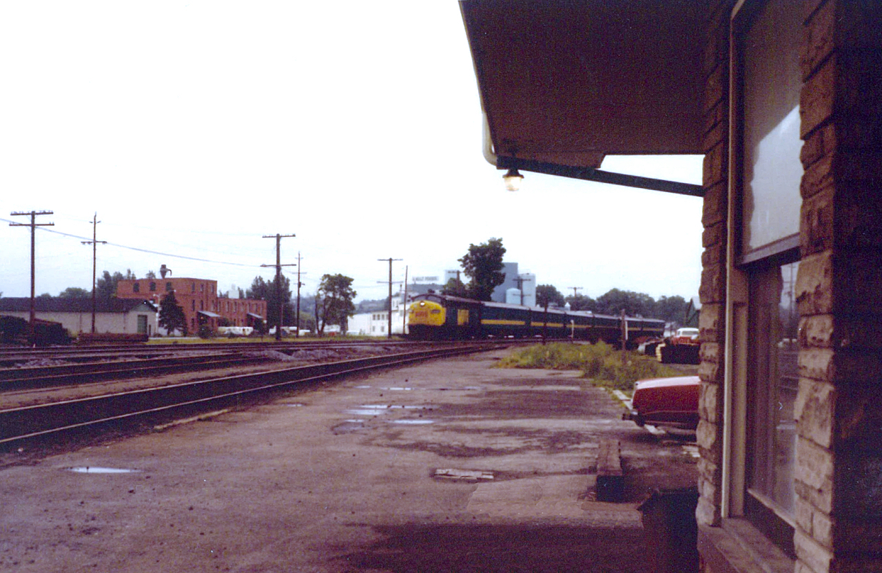 On a hot July afternoon one could feel the humidity after a brief downpour. Being only 4 years old at the time, my grandfather took this photo of a mid-afternoon VIA train, heading west to Toronto.

You will note that the two tracks in the foreground, is the 'actual' Kingston Sub. CN realigned the tracks due to the construction of the Centre Street underpass, and installed a temporary level crossing just behind us to divert traffic.