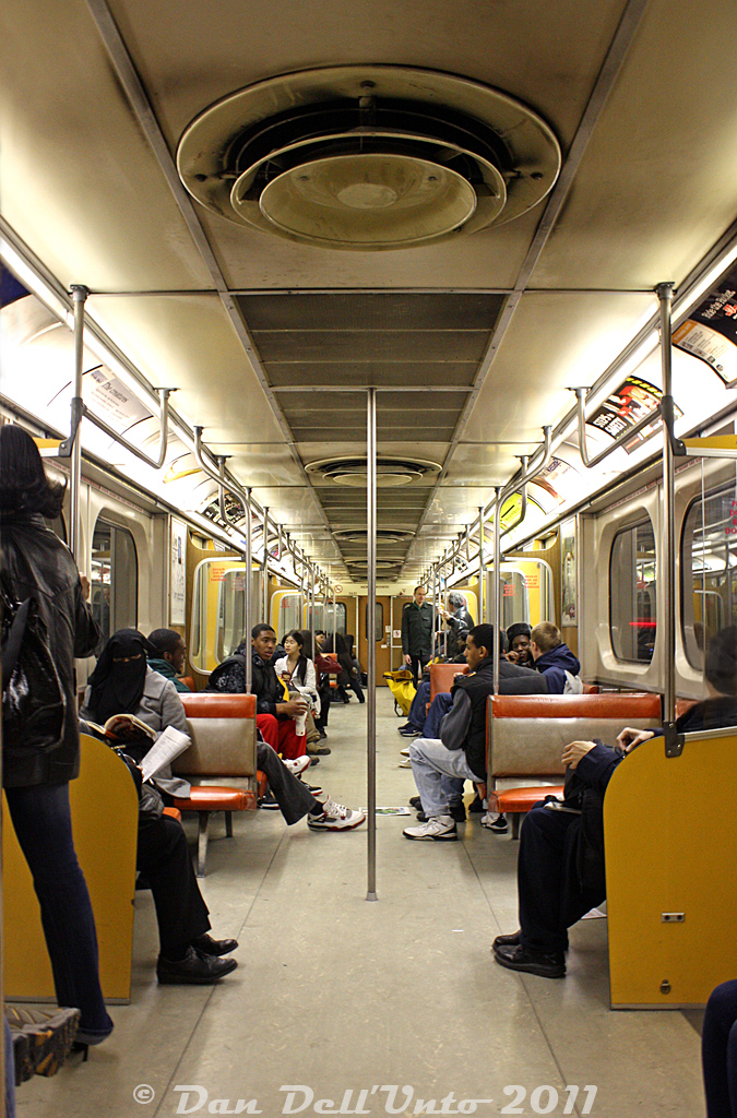 Here's some 1970's Retro Toronto goodness: the interior of TTC Hawker Siddeley Canada H4 5651, on a busy eastbound Bloor-Danforth train approaching Yonge Subway Station.Standard fare on your average H4 always included the comfy orange and grey bench seats, yellow doorways with cream doors, and the ol' simulated wood grain paneling. Shot portrait-style to show off the large distinct rooftop ventilator fans, at the time the last subway cars in service in Toronto with them (also found in old department stores like K-Mart). All the H1-H4 cars came with those fans, as well as the M1's, but their use was discontinued starting with the air-conditioned H5's. The early H's were also "camshaft control", so no buzzing like the later "chopper control" cars, just a whir on starting and stopping, and no air conditioning either. The final H4 train would run a few months later in January 2012.More H4 photos:Davisville Subway Station: http://www.railpictures.ca/?attachment_id=34861Christie Subway Station: http://www.railpictures.ca/?attachment_id=31197Keele Subway Station: http://www.railpictures.ca/?attachment_id=34662H4 ride (Youtube via another RP.ca contributor): https://www.youtube.com/watch?v=-rxna_nbkug