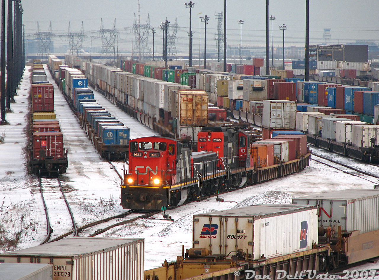 It was the day of the annual Toronto-area Christmas train show, held every November down at the Mississauga International Centre, but before pleasure there was business to attend to in Brampton: There had been a then-rare GMD-1 regularly assigned to the Brampton Intermodal Terminal set for switching the yard, and like Scooby Doo and the gang, we needed to go down and catch it.Departing around noon, after a visit to shoot a train on the BIT pullback track pulled all the way to Automatic Drive, the next stop was a visit to the Highway 7/Queen Street overpass. There was our target GMD-1 1423, visible in the yard but tucked away with her GP9RM-slug set on a track in the distance not doing anything (8-ball says crew lunch break). Since we weren't getting any action along Queen, a side-trip was made to the Malport Yard area to shoot CN #577 and #393, before doing some other shenanigans (probably lunch) and heading back to BIT for another look.Sure enough, 1423 with slug 242 and mother GP9RM 7265 were busy drilling cuts of intermodal cars at the north end of the yard, as other mainline trains yarded and did their switching. If this looks like a busy scene, it was - as CN's main Toronto-area container terminal, BIT is usually busy. Some photos were had, as 1423 had the significance of being the first GMD-1 built (CN 1000), before entering the late 80's rebuild program and emerging as GMD-1B 1423 (it's now preserved by the CRHA out west). The neat thing about shooting off Highway 7 is you can see part of Pearson Airport in the distance. Unfortunately was also really really cold and windy on that overpass, so this shot was not without sacrifice to the comfort of gloveless extremities.