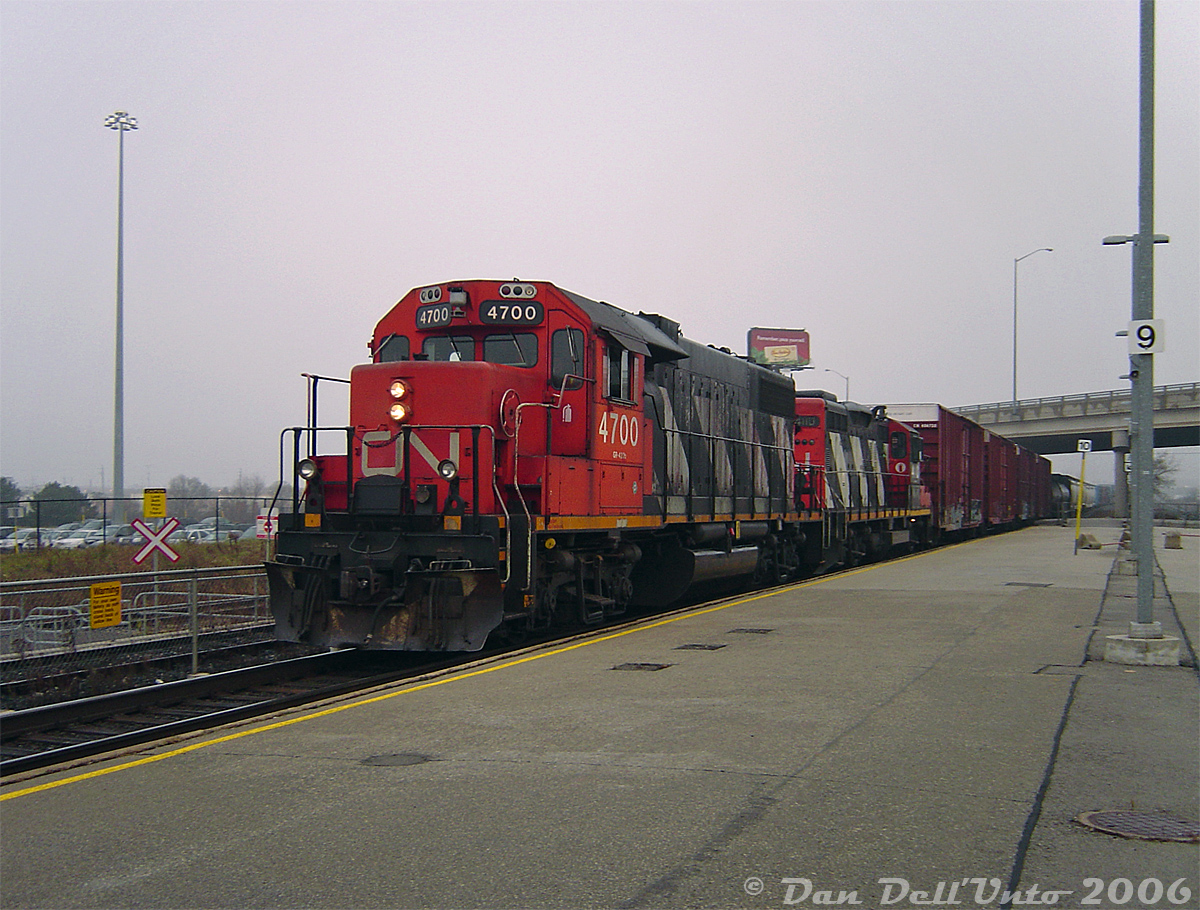 "That's not my GO train, where do I tap the Presto on this thing?!?!"

One redeeming feature of the chaos at Bramalea GO station was it would occasionally drop random CN trains like this out of nowhere into your lap. Waiting for a morning GO train? Here's a CN local finishing work around Brampton to shoot, or a GEXR export special with 10 brand new Class 66's fresh from London (that one actually happened). Witness CN GP38-2 4700 and GP9RM 4110 in matching zebra stripes showing up at 7:46am and slowly crawling through the morning fog, heading eastbound through Bramalea GO on track #2 with a sizable local in tow past everyone waiting for the next Toronto-bound GO train to appear. Usually the local working this area went through the other way in the mornings, so I can only speculate this was an overnight or early morning #578 that had finished switching some Brampton/Bramalea industries and was making its way back to Malport amid the morning GO rush, likely waiting for a gap in traffic so the RTC could give it the light through Halwest and into Malport Yard.

CN 4700 (ex-5500, the class unit) in ratty zebra stripes was a regular on the locals in the area at the time. Around 2007 it would depart and return in a fresh coat of the modern CN "website" livery.

The crossbucks and the weird railings next to 4700 were to corral the "Bramalea Marathon" runners safely over the unused Kuehne & Nagel siding by the south GO parking lot, known for multiple daily parking violations as spots filled up during the course of the day ("Fire route? Sorry, I need to catch the York University GO bus in 3 minutes or I'm late for that business finance exam at Schulich!"). Recent south parking lot renovations suggest this was all done away with, as most of the siding been removed prior.