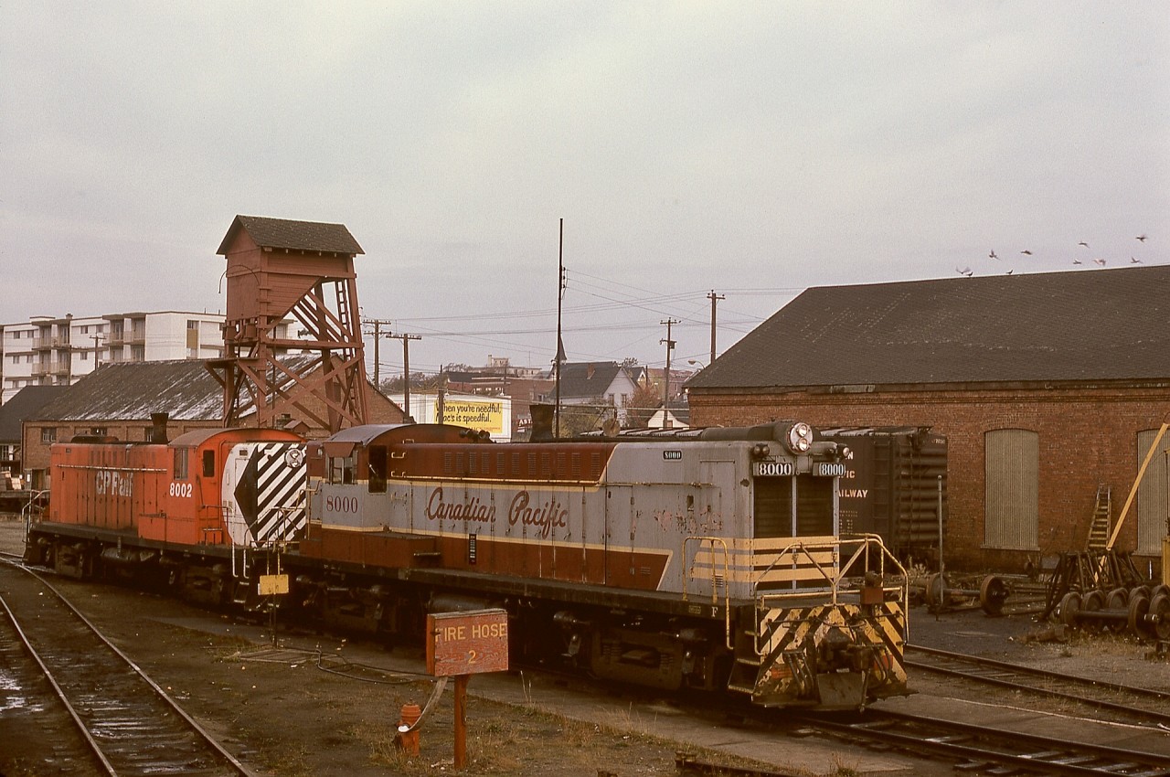 On the E&N shoptrack and sandhouse at Victoria on Thursday 1974-10-24, Baldwins CP 8000 and 8002 are ready to couple to northward freight train No. 51 to Stockett and down to Wellcox yard in Nanaimo.  CP 8000 survives and is being restored by the Railway Museum of British Columbia at Squamish, and the two brick buildings in this photo, stores on left and carshop on right, remain as part of a developing museum project in Victoria.  The sandhouse and CP 8002 are history.