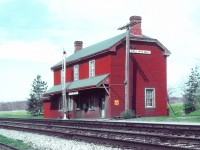 <b>For all Station Masters...</b>
<br>
<br>
CN Collins Bay station, circa late 50s or early 60s. Green shingled roof, well worn insulbrick that's starting to peel and fade, and a train order signal removed. 
<br>
<br>
Of interest...
<br>
<br>
Those who looked after the trains through this town always referred 'going down to the Bay', due to this section of mainline having many curves, on a grade. Behind the station, still looks empty with no sign of any suburb being built (today's Aylmer Crescent neighbourhood).
<br>
<br>
As time moved on, the decline in ridership continued, with the improvement of highways and the railways infrastructure to stay competitive. And with the new 'outer' Kingston station having been built with realignment away from the old <a href="http://www.railpictures.ca/?attachment_id=20777"> Montreal Street outer station </a> CN focused more on  eliminating the stops 'in between'. After all, the new station was built in a closer proximity to the stop in Collins Bay.
<br>
<br>
Thus, the end came around 1974 when the station was demolished. All that remains today, is a little avenue across from Edith Rankin United Church appropriately called 'Station St.' 
<br>
<br>
And it's at about this location, on the north side of the tracks being west of Collins Bay Road crossing, this large structure once stood. 
<br>
<br>
<i>Photographer Unknown, photo provided by the late Dave Savage, Canadian Railway Station News.</i>