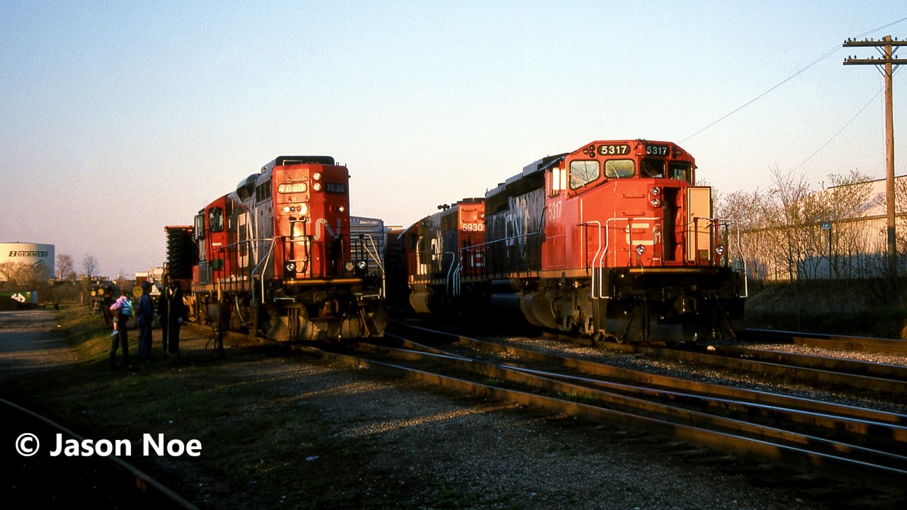 CN 395 is pictured in the yard at Kitchener, Ontario after taking the siding for VIA 89 and to lift the loaded auto frame cars seen to the left. Powering 395 are SD40-2(W) 5317 and GTW SD40-2 5930, which would soon begin lifting their cars, once the 15:30 Kitchener Job would clear the yard with GP9RM 7030. The auto frames were manufactured at the massive Budd automotive frame plant in Kitchener situated on the Huron Park Spur.