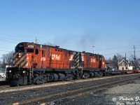 CP Rail C424 units 4205 and 4233 roll through downtown Brampton with the northbound "Moonlight" (train #89), crossing Queen Street and passing by the former CPR Brampton Station site, south of the <a href=http://www.railpictures.ca/?attachment_id=47463><b>diamond</b></a>. The <a href=http://www.railpictures.ca/?attachment_id=33072><b>old station</b></a> had previously been under threat of demolition by CP, but was disassembled and removed off-site for future preservation in 1981 by the local historical society. Despite the station's absence, the <a href=https://www.railpictures.ca/?attachment_id=53254><b>station grounds</b></a> here still had a passing track, back track, and ramp/team track. There once was a ramp just north of the station with its own siding, but at some point the old freight shed and loading platform on the right had been knocked down and converted to a ramp, and remained so into the <a href=http://www.railpictures.ca/?attachment_id=53272><b>OBRY era</b></a> (as did some of the siding tracks). <br><br>The three empty flatcars behind the power were likely bound for the <a href=http://www.railpictures.ca/?attachment_id=56690><b>Brampton Caterpillar plant</b></a> at Sandalwood Parkway near the Heart Lake community. The new Cat plant had opened two years prior in 1983 (its manufacturing operations had been moved from Cat's old Mississauga plant in the Dixie area) for the assembly of small rubber-tired loaders and logging skidders (often <a href=http://www.railpictures.ca/?attachment_id=57499><b>shipped out of the plant on flatcars</b></a>), but would close in 1992 during a round of plant consolidations due to the economic slump.<br><br>The 80's and 90's were a time for the C424's <a href=http://www.railpictures.ca/?attachment_id=38098><b>to shine</b></a> in branchline service, as part of CP's 10 Year Locomotive Program, they were modified from Diesel Road Freight (DRF) to Diesel Road Switcher (DRS) in the early 80's for service on branchlines as roadswitchers (along with the <a href=http://www.railpictures.ca/?attachment_id=35962><b>GP30</b></a> and <a href=http://www.railpictures.ca/?attachment_id=50381><b>GP35</b></a> units), to replace some of CP's aging 4-axle 1st generation GMD and MLW power either being rebuilt as yard units, or retired (<a href=http://www.railpictures.ca/?attachment_id=25402><b>brand new GP38-2 units</b></a> were also acquired to help with the displacement). The final C424 units were retired in 1998.<br><br>Flowerlea Dairy, in business at 6 Park Street on the left, was established in 1962 when a group of local milk producers purchased the old Pocock Dairy operations (est. 1920). They grew over the years and acquired Bolton Dairy in 1973, and also ran a distribution operation called Dairyland Transport Co-op. The Park Street location in downtown Brampton was their main milk bottling and distribution facility. Flowerlea's history is a little hard to trace in later years, but it appears its operations were sold to Saputo around 1993.<br><br><i>Peter Jobe photo, Dan Dell'Unto collection slide.</i>