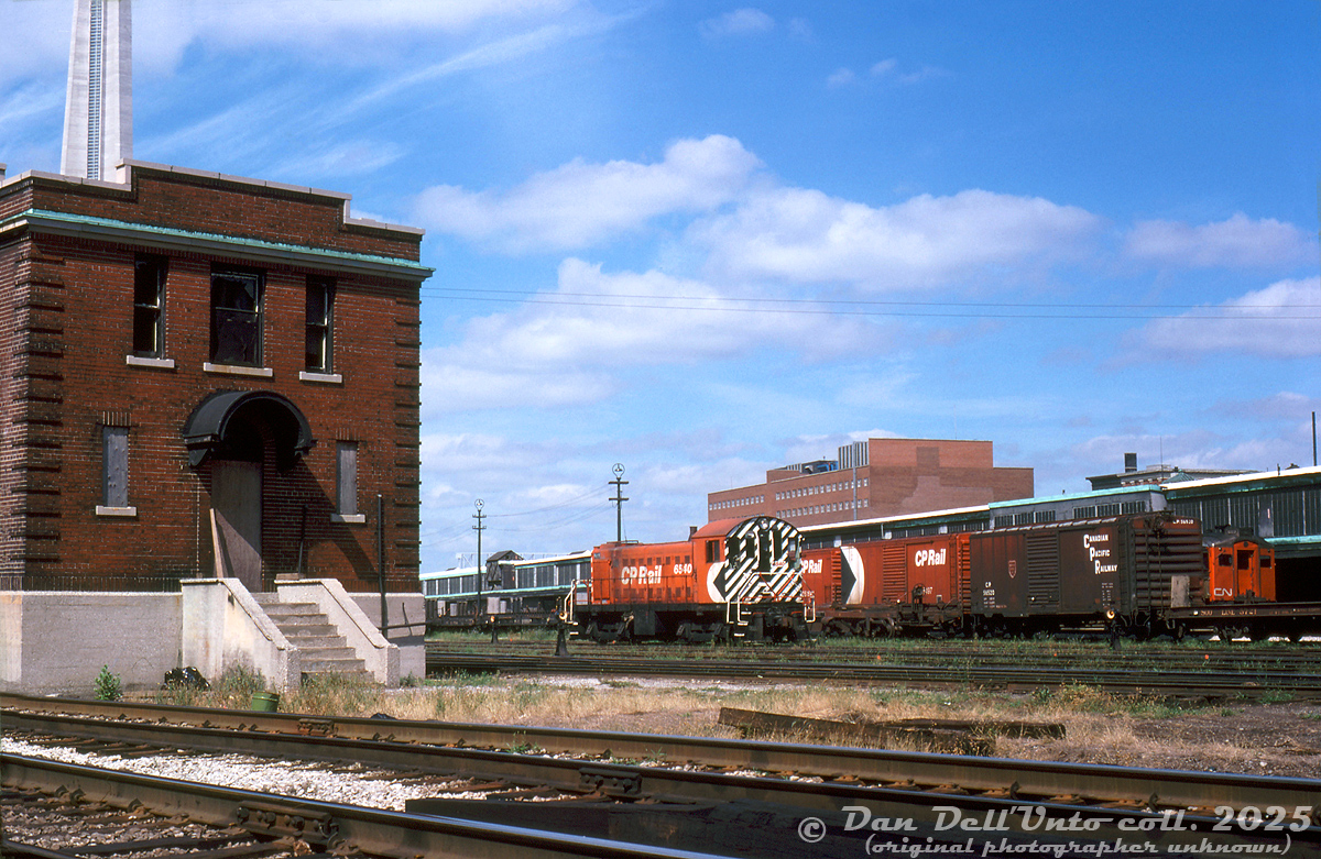 CP Rail MLW S3 6540 works the John Street coachyard area in downtown Toronto, seen next to the old CP yard office building, and the south end of Toronto Union Station's train shed near Bay Street subway/underpass. Some CP 40' boxcars and piggyback flatcars sit on the adjacent track (for the John St. piggyback ramps), and a set of CN RDC cars with RDC-1 6113 sit at the south end of the train shed on outside Track 9 (before the train shed extension was built for tracks 9 and 10).Few highrises are present on the Toronto skyline at this time, but the brown CNCP Telecommunications building is visible at 151 Front Street West.Bill Mischler photo, Dan Dell'Unto collection slide.