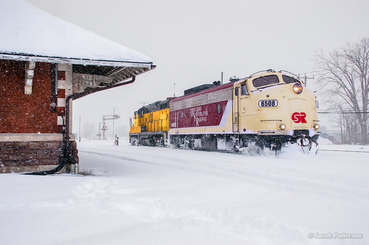 An afternoon snowstorm has blown in on OSR's Woodstock Job while working around its namesake town.  Cars have been pulled and spotted at the Roslin transload, and all outbound cars set out in the old Jellicoe yard tracks for CPKC to lift.  With freshly cleaned switches already filling back in, the crew takes their light power down to the east end of the yard, passing the 1899-built station, to lift inbound traffic.