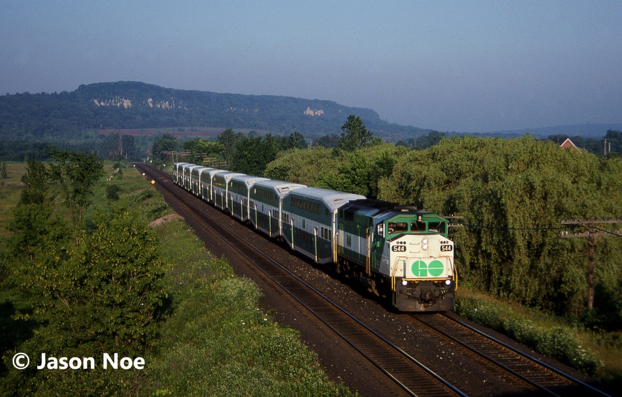 An early morning eastbound GO train is viewed entering Milton, Ontario on the CP Galt Subdivision where it will make it’s first station stop of the day, loading commuters for the trip into Toronto. At the time, all the GO trains on the CP line were based out of the Guelph Jct layover facility and every weekday morning, the eastbound parade of five empty train sets would descend the Niagara Escarpment into Milton about a half hour apart.