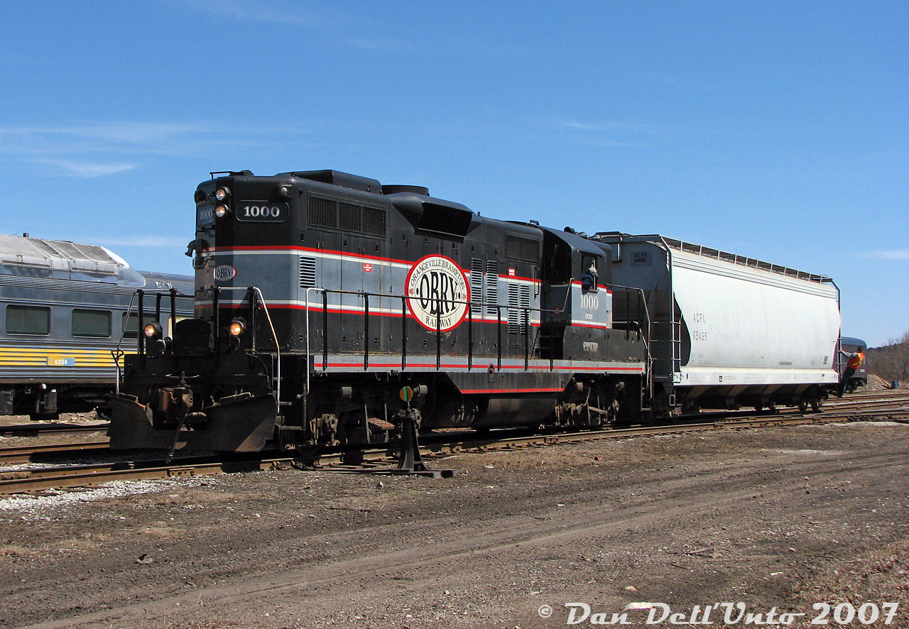 Even a shortline can be busy when there's work required. After their run up from Streetsville to interchange traffic, Orangeville-Brampton Railway's lone power, CCGX GP9 1000, switches the single hopper brought back on the return trip onto a cut of cars in the yard. Conductor Steve Bradley is diligently riding the end of the hopper to make the joint, while engineer Wayne leans out of the cab window and works the controls of his 1957 London-built steed. A fuel truck from the local fuel dealer would soon show up to fill the Geep, and after some light servicing by the crew, 1000 would be put away for the day. In the background, ex-VIA Rail RDC-9 6006 sits on the station track coupled to the rest of the Credit Valley Explorer consist, that was receiving some attention from a few individuals before its next upcoming tourist excursion.