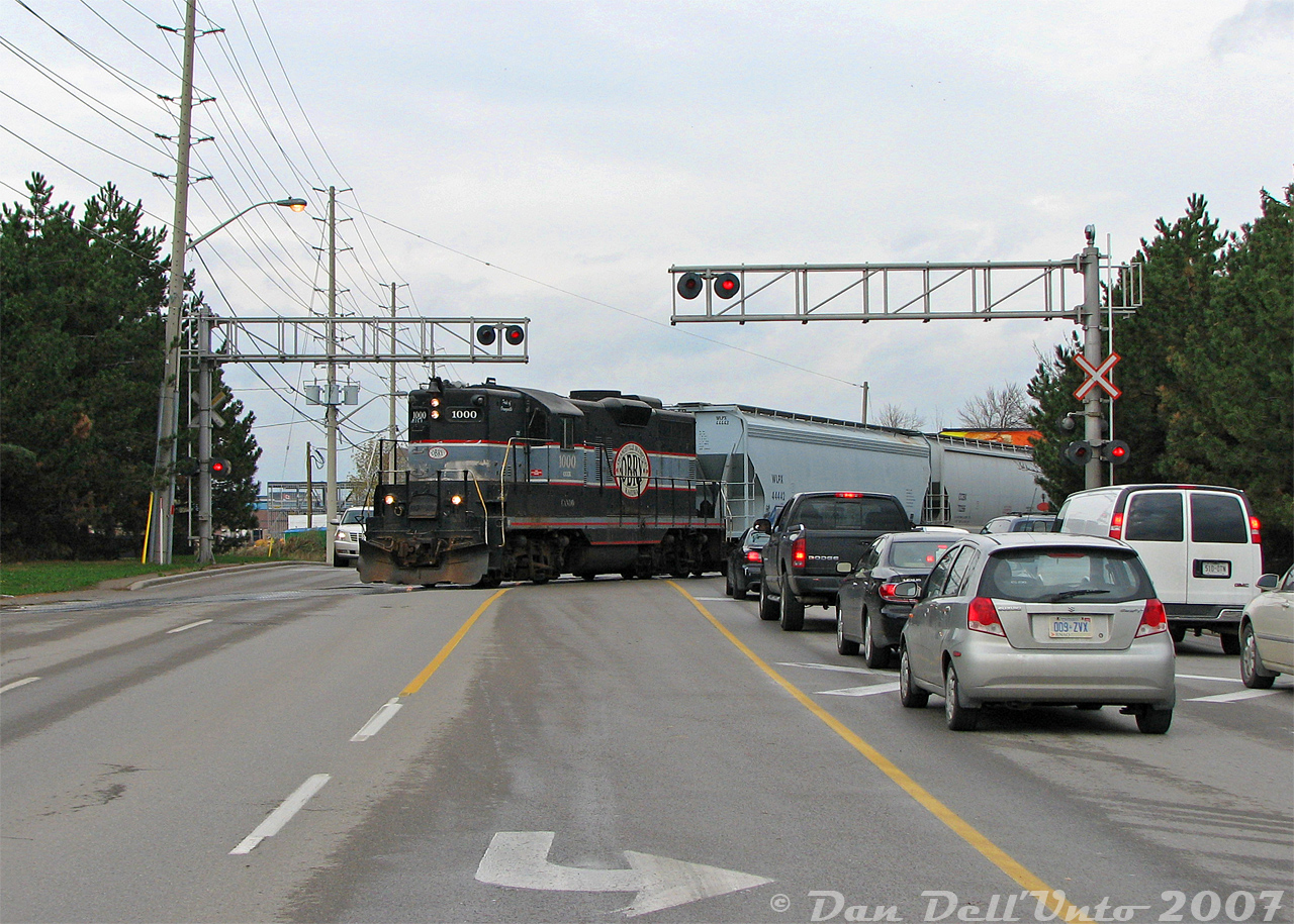 Orangeville-Brampton Railway's high-nose GP9 of choice, CCGX 1000, snarls traffic on Mississauga Road near downtown Streetsville as it switches the CP-OBRY interchange at Streetsville Junction. The unit is setting off its short train of 6 cars (two covered hoppers and four tank cars) before running around to the north end of the interchange track and lifting five covered hoppers for the trip back north.I had shot this train coming down through downtown Brampton down at the diamond, and beat it down to Streetsville just as it was arriving, nabbing it at Alpha Mills Road. Since the train was tying up Mississauga Road making its setoff, I remember I had to quickly loop around some of the side streets, swiftly park and bail out at the now-closed Streetsville Beer Store (there's a politician somewhere to blame for that), and then walk out into traffic for this quick "Don't get hit by a car today Dan" shot, as the Geep was just backing into the clear, I needed to be on the left side of the road, and oncoming traffic was getting impatient. After a few more photos here, it was back up to Brampton just in time for VIA #85 and the northbound OBRY run returning back to Orangeville (with no time for a quick stop at Credit Valley in downtown Streetsville for more Intermountain hoppers today).