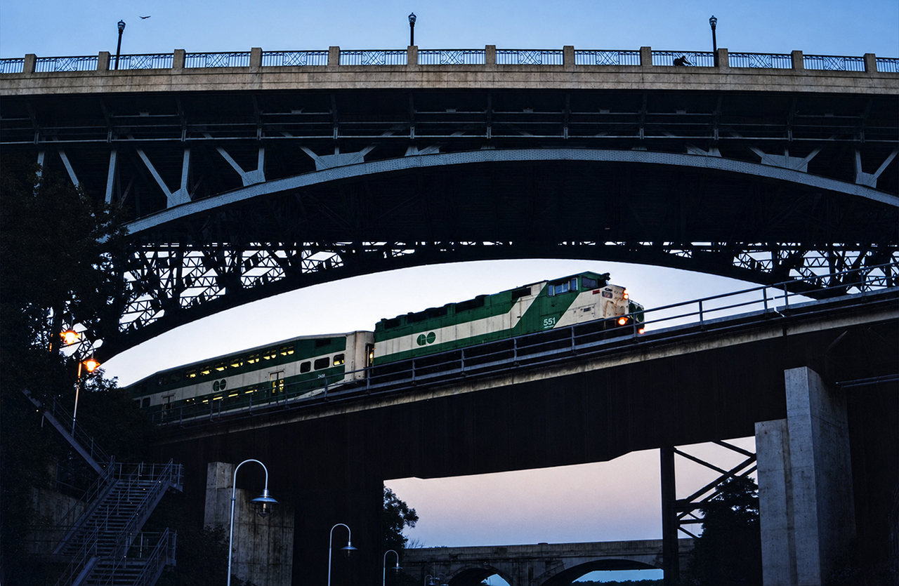 GO F59PH 551 brings an early morning rush hour train across the Desjardins Canal in Hamilton, on its way from Hamilton GO Centre to Toronto Union Station. This was a tricky shot to get with my Nikon F50 camera, as it was difficult to determine the correct aperture, speed settings and film type to capture the train without a blur in either the train or background from panning. The York Blvd. bridge is visible overhead, along with a bird and a biker on the way to their daily appointments. Highway 403 is in the background and the CN Grimsby/Oakville Sub directly behind me. It was a humid July morning, and the 551 was still in its factory paint shortly before its first overhaul.