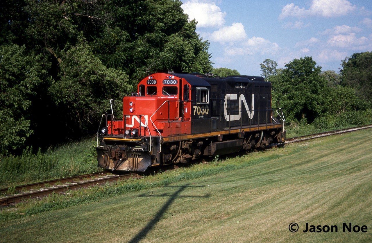 During a July evening, the CN 15:30 Kitchener Job with GP9RM 7030 has just crossed Queen Street on the Huron Park Spur and is pictured heading to the Budd Plant light power.