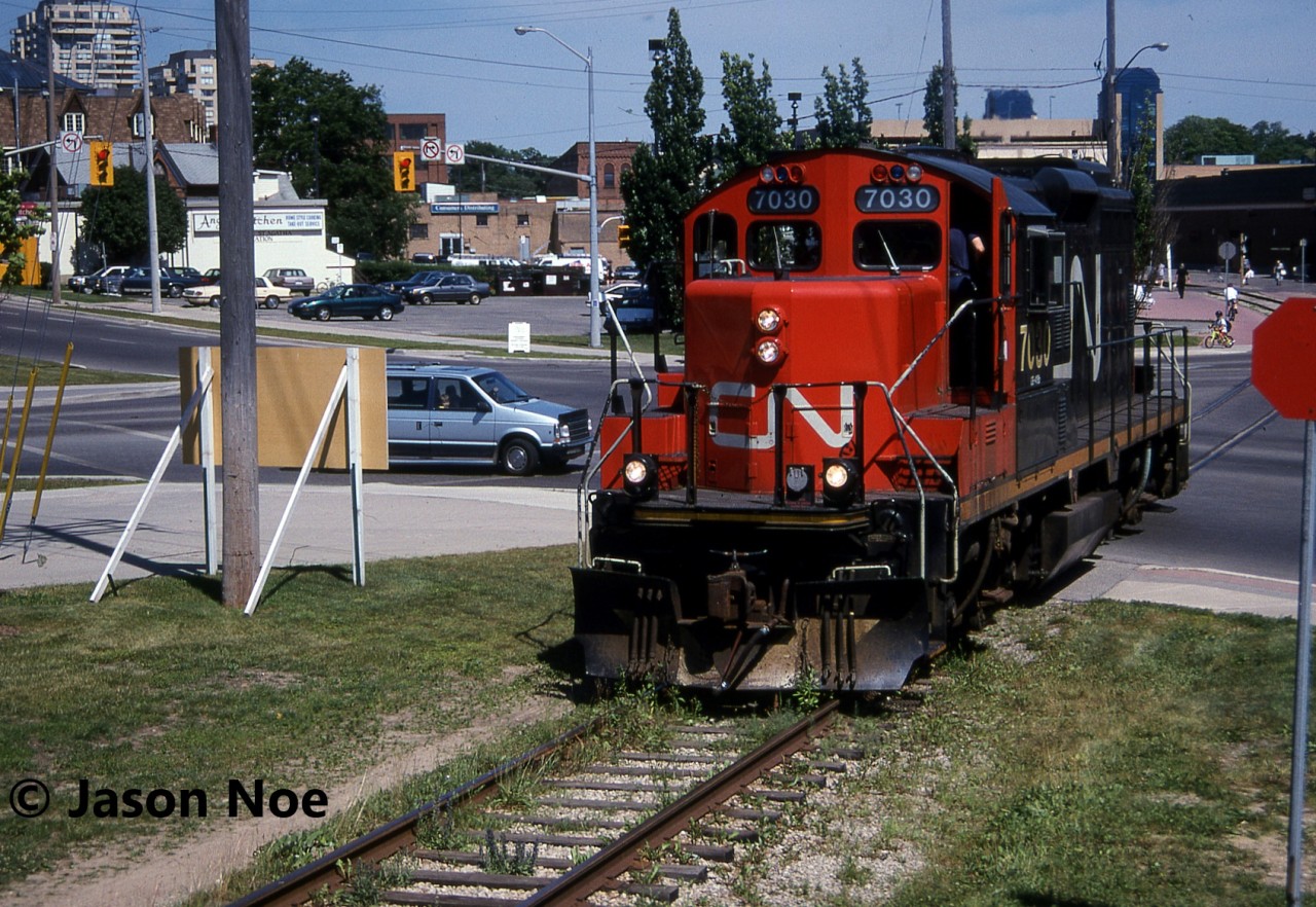 The CN 15:30 Kitchener Job with GP9RM 7030 makes a mid-afternoon appearance in downtown Waterloo, having just crossed Caroline and Erb Streets. The crew was heading to the town of Elmira, Ontario on the Waterloo Spur light power. Often during the month of July in the 90’s, with the Budd Plant in Kitchener slowing production for summer shut down, they didn’t require CN service daily, so the 15:30 Job would head to Elmira earlier in the afternoon rather than later in the evening.