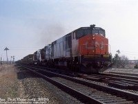 CN HR616 2116, one of Bombardier's short-lived line of "High Reliability" (hah) locomotives, leads a 2000-series C630M and 2300-series M636 on a westbound freight on the Halton Sub, seen crossing Torbram Road and advancing through Halwest (the junction between CN's Halton and Weston Subs) on the Brampton-Missisauga border. The Halton-Weston connecting track can be seen to the right of the 2116, as well as the overhead crane in the background for the MakSteel facility next to <a href=https://www.railpictures.ca/?attachment_id=59663><b>Malport Yard</b></a>.<br><br>On the left, out of view in the field next to the photographer, there was once a lumber yard back in the 70's called Lampton Lumber with a siding, that has since all but vanished. There were once about four lumber yards in this immediate area of Bramalea back in the more rural days (see aerials <a href=https://www.toronto.ca/ext/archives/s0012/fl1971/s0012_fl1971_it0235.jpg><b>here</b></a> and <a href=https://www.toronto.ca/ext/archives/s0012/fl1971/s0012_fl1971_it0234.jpg><b>here</b></a>), all with rail sidings: Lampton Lumber here,  Weston Road Lumber on the other side of the tracks to the south (still present today as Weston Forest Products), Malton Lumber (ex-Reid & Co./Lauder Boake Lumber) off Bramalea Road immediately south of Halwest, and Cashway Lumber (L.W. Larkin) that used to be at the present Bramalea GO station site. The encroachment of one-stop-shop big box building improvement stores such as Aikenheads, Home Depot and Lowes in the 90's no doubt contributed to the decline of the local small-town lumber yards.<br><br><i>Original photographer unknown, Dan Dell'Unto collection slide.</i><br><br>(This unlabeled slide (possibly taken by the late Keith Hansen) had no location given, but sometimes one just recognizes a spot).