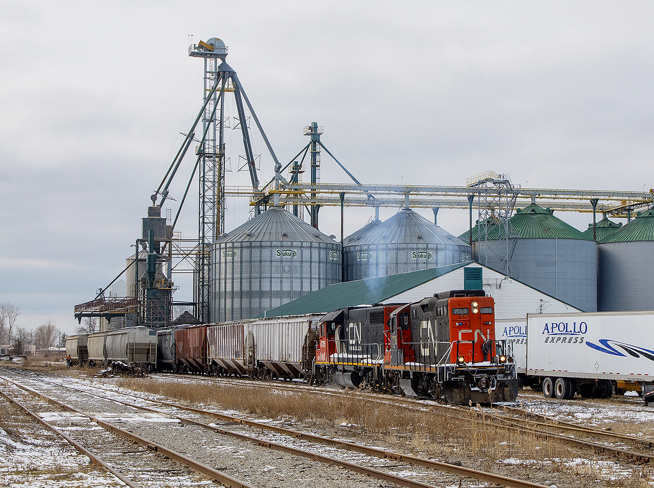Part One - ARRIVAL OF 514 


On a cold and bitter January day, the sun was peaking out, but in very short spurts.
Both 7068 and 4705 went right to work. With a larger than normal cut of cars, both engines were working hard, switching out the large ADM facility. To the right, the trucks sit for the Apollo Group (property management and other services, I assume for moving?). Kind of ironic, that increased truck usage would ultimately reduce rail traffic. Nonetheless, these trailers are idle this day.


To the left (and out of frame), are two items now since removed. See that wooden walkway that crosses both tracks? This is where the old C&O Blenheim station once stood (you can see Bill Thomson's photo by   clicking here.  Also, the former Thompsons facility (now the Anderson's). They had an  old tonner,  that until recently sat on one of the sidings within the property.