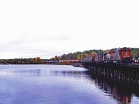 As northwestern Ontario's fall colours turn, CN's last SD40 leads a sister across the bridge at Windy Point (east of Fort Frances) on a cool, cloudy day in 1983. Train 408 is operating from Winnipeg's Symington Yard to Thunder Bay's Neebing Yard with a consist typical of the era--40 foot grain box cars, covered hoppers of grain, and various other merchandise traffic. At this time, pairs of "international service" SD40s powered most trains, including those to the Duluth, Winnipeg and Pacific which turn south at Duluth Jct about 10 miles west of here.