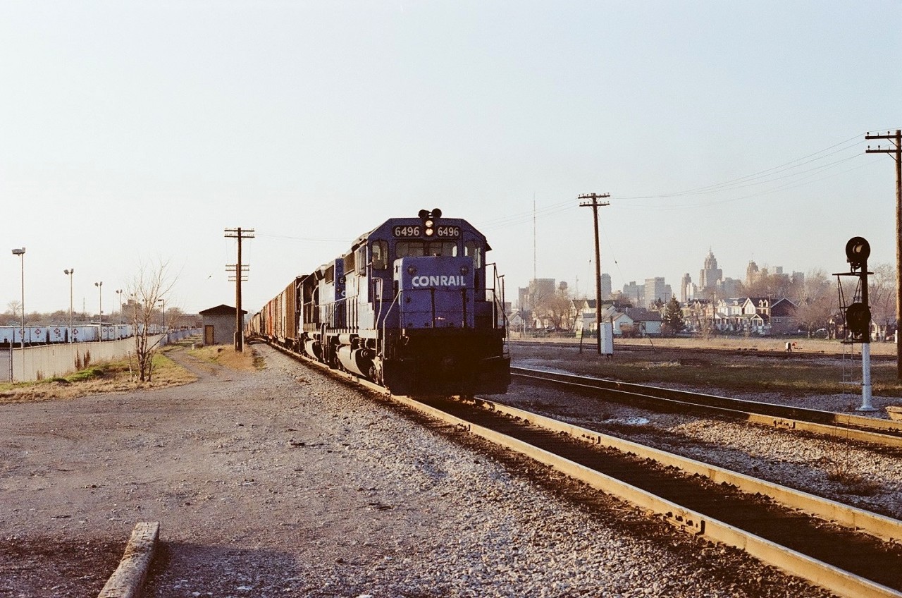 The cross-border transfer from Detroit's Livernois Yard - Conrail symbol LW-30a - is pulling hard up the grade out of the Detroit River tunnel. Just beyond the classic Michigan Central station, he will swing left through the crossover and continue to the yard. 
The mixed skyline in the distance is Windsor and Detroit, while to the left of the train, trucking company International Cartage has a healthy fleet of trailers.
Inside of 4 years this will become CN Windsor South and CR will have exited Ontario.
ETTS.
