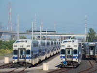 Stored bilevel cars are parked at EXO's maintenance yard in Pointe St-Charles as an REM train passes in the background.