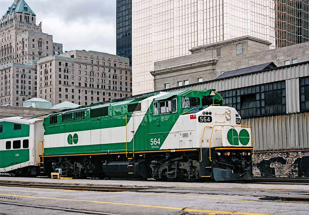 GO F59PH 564 departs Toronto Union Station eastbound towards Pickering. It is a cold and cloudy Christmas Eve of 1997, and the 564 was recently put back into service after a lengthy time in storage. It remains GO's newest F59PH, after sisters 565-568 were sold to Trinity Railway Express (TRE) in Dallas, Texas amid provincial government cutbacks of the mid-1990s. Despite only being built in 1994, units 562-564 were kept in long-term storage at Willowbrook, along with sisters 520-523 before being placed back into service shortly before this image was taken. This is another photo location that is no longer possible, due to the buildout and modernization of Union Station and surrounding area. The Royal York Hotel still stands, but the historic train shed in the background has long since been leveled.