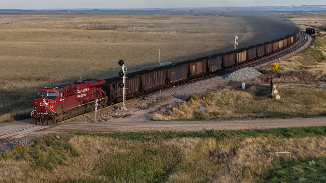 The coal dust is flying as CPKC 820-902 highballs through MacKid, Saskatchewan.  In the distance, the elevator at Maple Creek can be seen, across an otherwise empty prairie.  Coal trains on the prairies are rather rare, with only a handful a year operating to Thunder Bay.