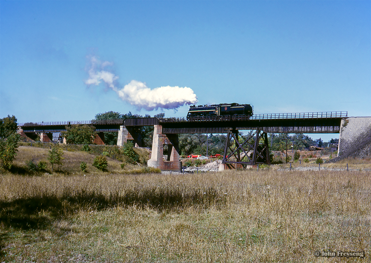 The weekend of September 13 - 15, 1963 marked a massive undertaking by the Upper Canada Railway Society, a 692.2 mile excursion from Toronto - Ottawa - North Bay - Temagami - Toronto, with seventeen coaches behind CNR 6167. With the train having run overnight from Toronto - Ottawa on the 13th, the train turned west and departed the nation's capital early on the 14th, running across northern Ontario to North Bay. 6167 would be removed at North Bay, with ONR FP7s handling the train to Temagami overnight. The consist returned to North Bay on the morning of the 15th, with 6167 taking over once again for the return to Toronto.  Further information can also be found in the December 1963 UCRS news letter.

About 40 miles after the previous runpast, CNR 6167 has cut off from the excursion to take on coal and water, and is seen making a reverse move over the Muskrat River bridge.  Below the bridge, and to the right of the tender, note the white milepost of the CNR Locksley Subdivision, which should be mile 20, as "National Junction" would be located at mile 20.2, off to the right closer to town.  The Locksley Sub ran 21.1 miles from Golden Lake, and a connection to the CNR Renfrew Sub, north to Pembroke, ending at a downtown station.  CNR was permitted to abandon the Locksley Sub from Golden Lake to mile 19.5 in 1960, and mile 19.5 - mile 20.01 in 1963.  The remaining mile was used as an industrial spur.

Pembroke was served by another CNR station on the mainline, a bit east of this location.  Del Rosamond shot an eastbound there in 1958.

Scan and editing by Jacob Patterson.
