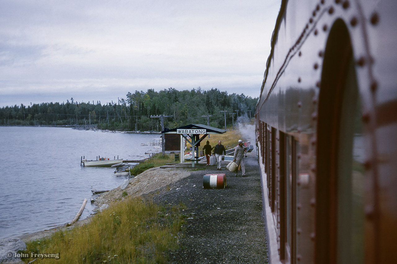 Algoma Central Railway train 2, running Hearst - Sault St. Marie, pauses at Wabatong near mile 207.  Passengers are seen gathering their belongings from beneath the shelter on the shore of Wabatongushi Lake, passing them to the baggage handler before climbing aboard.

Pausing at Oba
The head end
ACR meets CN
New GP35s
South of Mosher

Scan and editing by Jacob Patterson.