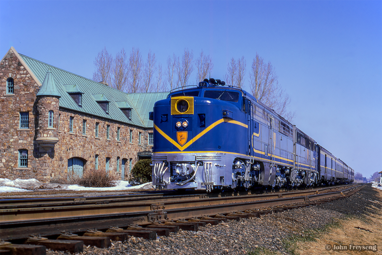 Operating Montreal – New York, Delaware & Hudson train 34, The Laurentian, pauses in front of the Napierville Junction Railway station at Lacolle, Quebec.  Built in 1930, this structure served as a station and customs office for the NJR and later the D&H.

The D&H had operated passenger service into Montreal since 1923 with both its Laurentian by day and Montreal Limited overnight. These operated into Canada over D&H subsidiary, Napierville Junction Railway, running 27 miles from Rouses Point, New York - Delson and into Montreal via CPR trackage rights. Endangered by declining ridership by the 1960s, new management in the D&H's passenger department sought to revitalize the operation after negative public response to the potential cancellation. To do so, the D&H acquired four ALCO PA-1 locomotives in 1967, numbered 16 - 19, from the ATSF. Wearing a modified ATSF Warbonnet scheme, with D&H blue replacing the red, they would handle the trains of second hand equipment until their final runs on April 30, 1971, as neither The Laurentian or Montreal Limited were included in Amtrak's start up.  In 1974, passenger service over the D&H was to be resurrected by Amtrak as The Adirondack, funded by the New York Department of Transportation. With limited equipment available to Amtrak at the time, the D&H, then led by Carl Sterzing, provided its PAs and passenger equipment for the runs. For their return to passenger operation the PAs would be rebuilt from their original ALCO 244 prime mover to ALCO 251s in 1974 by Morrison-Knudsen, and designated ALCO PA-4s. The rebuilt units served until 1977 when Amtrak replaced the D&H equipment with Rohr Turboliners. It is also noted, the D&H had acquired a fifth PA for parts in the 1960s, former New Haven 0783. It was scraped in 1972.

The last passenger train to stop at Lacolle would be in April 1985, when Amtrak’s Adirondak was rerouted from CP Windsor Station to CN/VIA Rail Gare Centrale, taking CN’s Rouses Point Subdivision through Cantic a few miles to the east.  Lacolle station still stands today, designated a heritage railway station in 1991.

More D&H PA Canadian action:
D&H 16 near Montreal West
D&H 18 at Montreal West
D&H 18 at Westmount
Windsor Station 1975

Scan and editing by Jacob Patterson.
