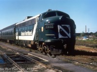 Here's a nice GO Transit locomotive on the head end of its GO train at GO's Willowbrook Yard: Ontario Northland FP7 1517! Back when GO first launched, they planned to expand to full service in September 1967 using some of their ordered-but-not-yet-delivered <a href=http://www.railpictures.ca/?attachment_id=32352><b>self-powered Hawker Siddeley cars</b></a> (D100-D108, later <a href=https://www.railpictures.ca/?attachment_id=60141><b>9825-9833</b></a>) to cover those runs. Unfortunately, those cars were late to be delivered, and since they were a new design of unknown reliability, had to be tested and troubleshot before being put into service (and according to the old "Building GO Transit" article there were problems, notably with the English-made Rolls-Royce engines constantly shutting down). So as an interim measure, the Ontario government borrowed two sets of conventional trains from Ontario Northland, composed of an FP7 at each end of 5 or so older coaches.<br><br>GO experimented with various configurations, including both FP7's at one end, and one FP7 per end but only one powering the train in each direction, and determined both units had to be online and providing power to maintain the tight commuter schedules. The solution reached was an FP7 at both ends connected with long MU cables running along the coaches, enabling both units to be online and respond as one. The two Ontario Northland consists operated in GO service during 1967-1968. Two "Progressive" paint scheme units (<a href=http://www.railpictures.ca/?attachment_id=33549><b>1517</b></a> and <a href=http://www.railpictures.ca/?attachment_id=38638><b>1521</b></a>) were among the ONR FP7's that did time on these trains. The self-powered cars coming online and a follow-up order for 14 more unpowered coaches in 1968 seemed to alleviate the equipment shortage, and the ONR consists were returned.<br><br>The self-powered cars proved to be more troublesome than they were worth, and GO neutered them by depowering all nine and converting them into regular cab cars. Some of those Ontario Northland F's would come back in the 70's as unpowered control cab/generator cars (APCU's), rebuilt for GO by Ontario Northland.<br><br>This photo spot is around the northeast end of the old Willowbrook Yard shop buildings (the former <a href=http://www.railpictures.ca/?attachment_id=32164><b>CN Mimico Yard</b></a> car repair shop that GO originally took over) just east of present-day Islington Avenue, where the UPX servicing shop is today. The blue pickup truck in the background sits by a CN service track that ran along the north end of the yard, formerly CN's Oakville Sub mainline right-of-way until it was relocated to the middle of the yards concurrent with GO establishing facilities here. In the far distance are the old Ontario Ministry of Transport buildings that were used for ambulance upfitting for sale to municipalities across the province for many decades.<br><br><i>Original photographer unknown, Dan Dell'Unto collection slide (duplicate).</i>